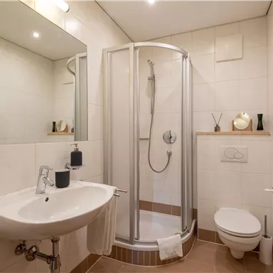 Ein modernes Badezimmer mit einer Dusche, einem Waschbecken und einem WC. Die Wände sind hell gefliest und es gibt eine komfortable Ausstattung.