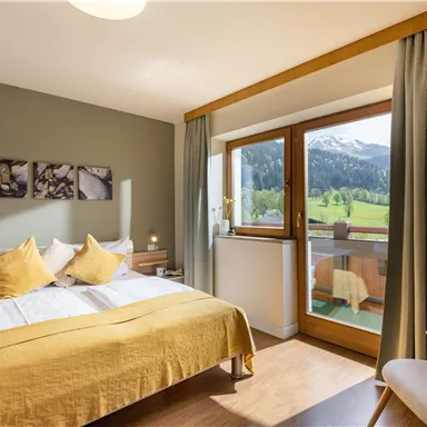 Ein gemütliches Schlafzimmer mit einem großen Bett und gelben Kissen. Der Raum hat ein Fenster mit Blick auf eine grüne Landschaft und Berge.