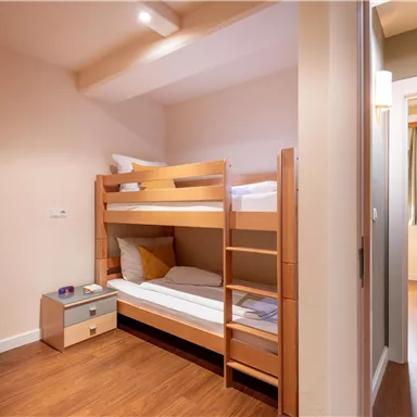 Ein kleines Zimmer mit einem Etagenbett und einem Nachttisch. Das Zimmer hat einen hellen und modernen Stil mit Holzfußboden.