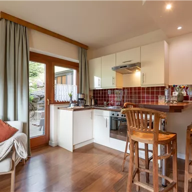 Eine moderne Küche mit Holzfußboden und roten Kacheln. Es gibt eine Essbar mit Hochstühlen und einen Aussicht auf den Garten durch die Tür.