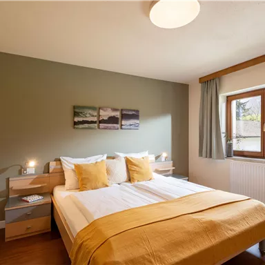 Ein modernes Schlafzimmer mit einem großen Bett und gelben Kissen. Die Wände sind in beruhigenden Tönen gehalten und es gibt ein Fenster mit Blick ins Freie.