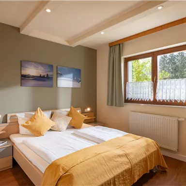 Ein gemütliches Schlafzimmer mit einem Doppelbett und eleganter Bettwäsche. Das Zimmer hat große Fenster und minimalistische Dekoration an den Wänden.