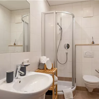 Ein modernes Badezimmer mit einer Duscheinheit und einem Waschbecken. Die helle Ausstattung sorgt für eine angenehme Atmosphäre.