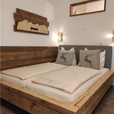 Ein gemütliches Schlafzimmer mit einem großen Holzbett und dekorativen Kissen. Die Wände sind in hellen Farben gehalten, und es gibt eine Holzkunst an der Wand.