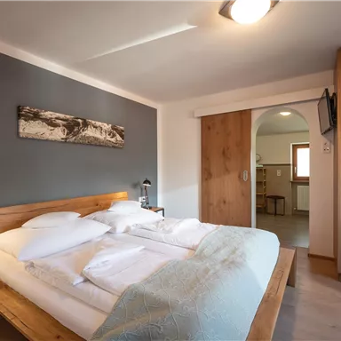 Ein modernes Schlafzimmer mit einem Doppelbett und Holzdetails. Die Wände sind in neutralen Tönen gehalten, und es gibt einen Zugang zu einer kleinen Küche.