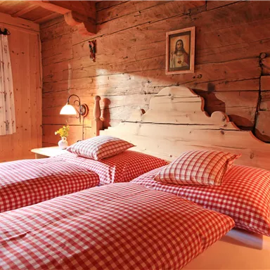 Ein gemütliches Schlafzimmer mit zwei Einzelbetten, die mit karierten Bettdecken ausgestattet sind. Die Wände sind aus Holz, und ein Fenster lässt warmes Licht herein.