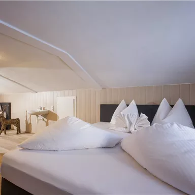 Ein gemütliches Schlafzimmer unter dem Dach mit zwei Betten und weißen Kissen. Es gibt einen kleinen Tisch und einen Stuhl im Raum.