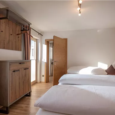 A modern room with two single beds and wood paneling. Large windows and bright colors create an inviting atmosphere.