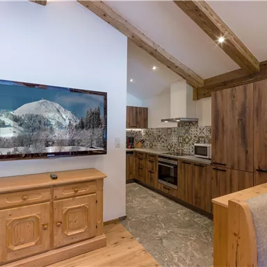 Eine moderne Küche mit Holzoberflächen und einem großen Fernseher an der Wand. Der Raum hat eine gemütliche Atmosphäre mit einem hellen, offenen Design.