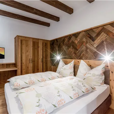 Ein gemütliches Schlafzimmer mit einem Doppelbett und geschmackvollen Kissen. Die Holzvertäfelung und der Fernseher sorgen für eine angenehme Atmosphäre.