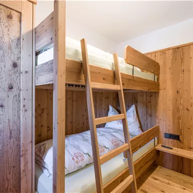 Ein gemütliches Zimmer mit einem Etagenbett aus Holz. Die Wände sind ebenfalls aus Holz, was eine warme Atmosphäre schafft.