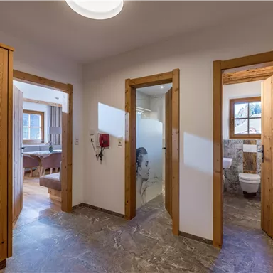 Ein heller Flur mit Holzverkleidung und mehreren Türen. Zu sehen sind ein Badezimmer und andere Räume im Hintergrund.