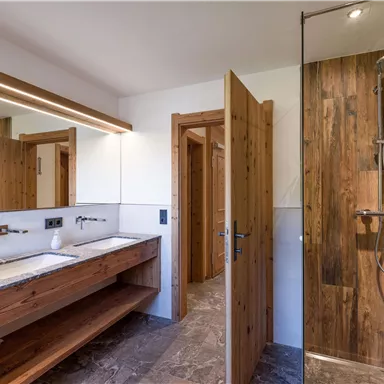 Ein modernes Badezimmer mit Holzdetails und einer Dusche aus Glas. Der Raum ist hell und gepflegt, mit einem eleganten Waschbecken.