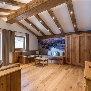Eine gemütliche Wohnung mit Holzbalkendecke und modernen Möbeln. Ein großen Fenster bietet einen Blick auf die Natur draußen.