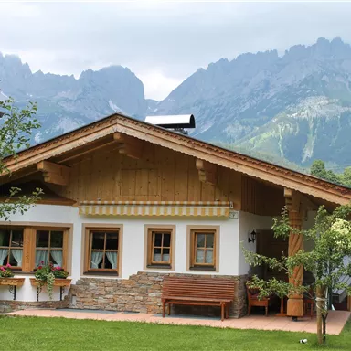 A cozy wooden house with a beautiful garden. Majestic mountains rise in the background.