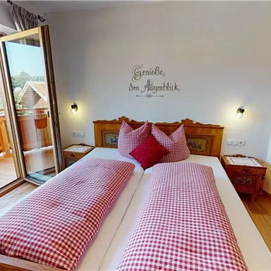 A cozy bedroom with a large window and access to the balcony. The beds are decorated with red checkered pillows.