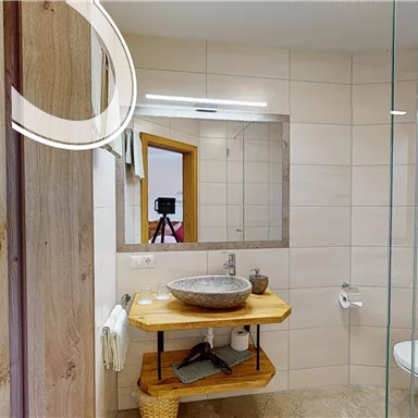 A modern bathroom with a large mirror and an elegant sink on a wooden shelf. The walls are light tiled and the decor is simple and appealing.