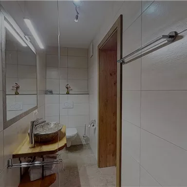 A modern bathroom with white tiles and wooden details. It features a sink, a mirror, and a toilet.