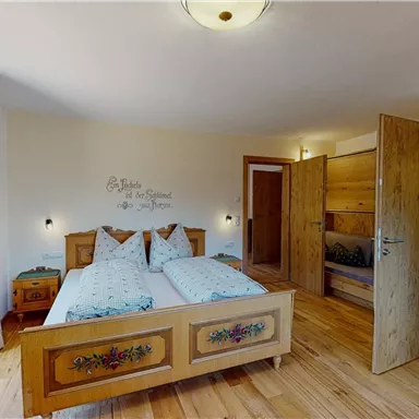 A cozy bedroom with wooden floors and a large bed. The walls are painted light and decorated with a charming wall design.