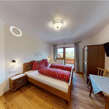 A cozy bedroom with two single beds and red patterned bedcovers. The room features a window with a view and a small seating area.