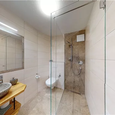 A modern bathroom with a glass shower and a stylish sink. The walls are tiled in neutral tones, creating a bright, inviting atmosphere.