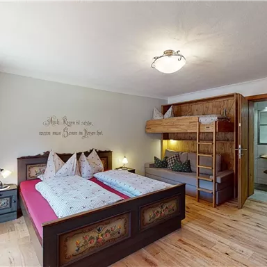 A cozy bedroom with a double bed and a bunk bed. The wooden ceiling and wooden floor give the room a warm atmosphere.