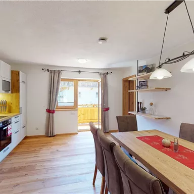 A modern kitchen with a wooden dining area. There are large windows that provide plenty of daylight.