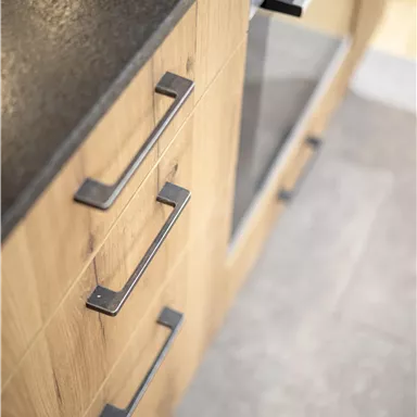 A modern kitchenette with wooden fronts and a black countertop. The furniture is designed to be simple and functional.