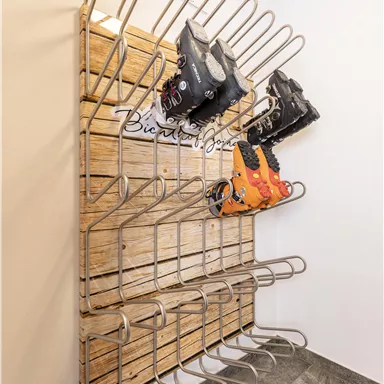A stylish frame made of wood and metal for storing ski boots. Several compartments are visible, in which some boots are placed.