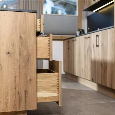 A modern kitchen with wooden cabinets and open drawers. The floor is tiled with gray tiles.