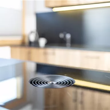 A modern kitchen with a black countertop. In the foreground, a round drain is visible.