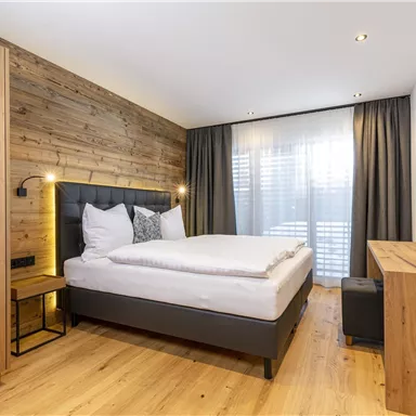 Ein modernes Schlafzimmer mit Holzwänden und einem gemütlichen Bett. Große Fenster bieten viel Tageslicht und eine warme Atmosphäre.