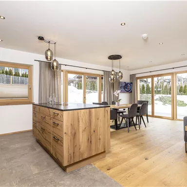 A modern kitchen with a wood island and plenty of natural light. The space is bright and inviting, with a dining table and a cozy living area.