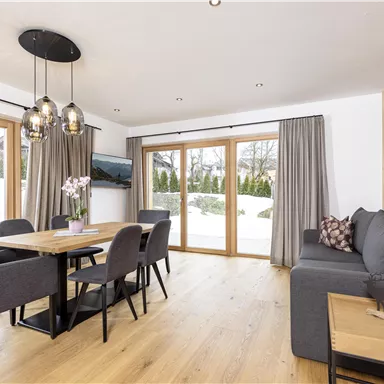A modern dining room with a wooden table and comfortable chairs. Large windows offer a view of the snowy landscape.