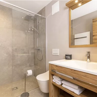 Ein modernes Badezimmer mit einer Glasdusche und einer Holzwaschbecken. Es sind frische Handtücher und eine stilvolle Beleuchtung vorhanden.