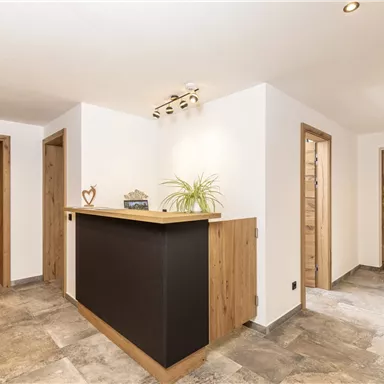 Ein moderner Empfangsbereich mit einem Holztheke und weißen Wänden. Die Umgebung ist hell und freundlich mit einem eleganten Fußboden.