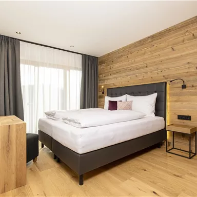 Ein modernes Schlafzimmer mit Holzverkleidung und einem großen Fenster. Das Zimmer ist hell und gemütlich eingerichtet, mit einem komfortablen Bett und eleganten Möbeln.