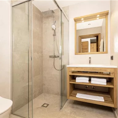 Ein modernes Badezimmer mit einer Glasdusche und einem Holzwaschtisch. Es gibt handtücherbare Regale und einen großen Spiegel.