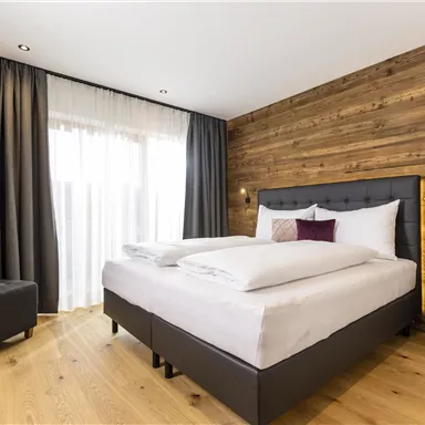 Ein modernes Zimmer mit einem großen Bett und Holzverkleidung. Große Fenster lassen viel Licht hereinscheinen.