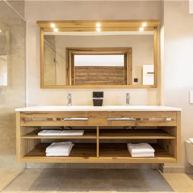Ein modernes Badezimmer mit einer Holzwaschtischanlage und großen Spiegeln. Die Dusche ist offen und der Raum wirkt hell und einladend.