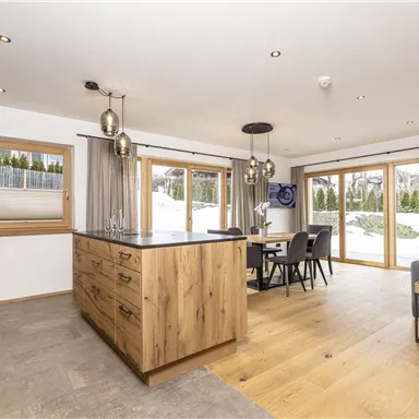 Eine moderne Küche mit Holzschränken und einem großen Kücheninseln. Große Fenster bieten einen Blick auf die Schnee-Landschaft draußen.