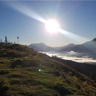 A picturesque mountain landscape with the sun rising over the peaks. The sky is clear and the fog lies gently in the valley.