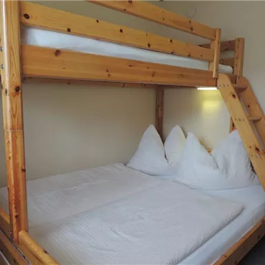 Ein einfaches Etagenbett aus Holz mit zwei matratzengestellten Schlafplätzen. Die Bettwäsche ist sauber und ordentlich, und es gibt zwei große Kopfkissen.