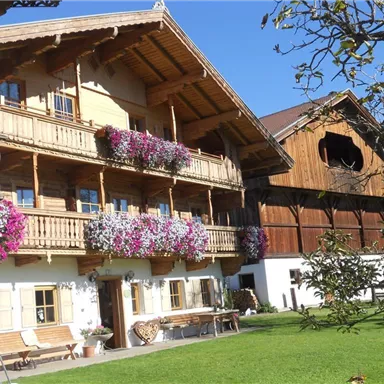 Ein traditionelles Holzhaus mit Balkonen, die mit bunten Blumen geschmückt sind. Im Vordergrund befindet sich ein gepflegter Garten.