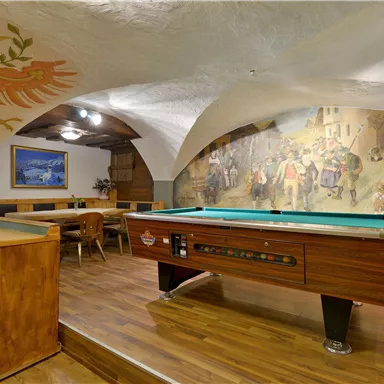 Ein gemütlicher Raum mit einem Billardtisch und bunten Wandmalereien. Die Holzdecke und der Boden strahlen Wärme aus.