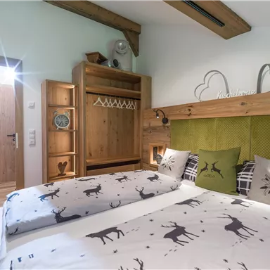 Ein gemütliches Schlafzimmer mit einem Doppelbett und Holzverkleidung. Die Wände sind in natürlichen Tönen gehalten, und das Bettzeug ist mit einem Hirschmotiv verziert.