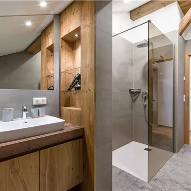 Ein modernes Badezimmer mit Holz- und Steinakzenten. Es verfügt über eine Dusche, ein Waschbecken und frische Handtücher.