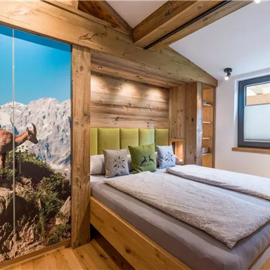 Ein modernes Schlafzimmer mit Holzelementen und einem großen Bett. An der Wand ist ein Bild einer Berglandschaft mit einem Steinbock zu sehen.