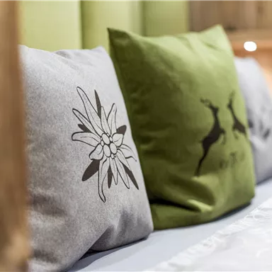 Kissen mit unterschiedlichen Designs liegen auf einem Bett. Die Farben sind sanft und verleihen dem Raum eine einladende Atmosphäre.