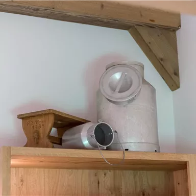 Ein vintage Melker und eine kleine Holzbank stehen auf einem Regal. Im Hintergrund sind holzähnliche Wände zu sehen.